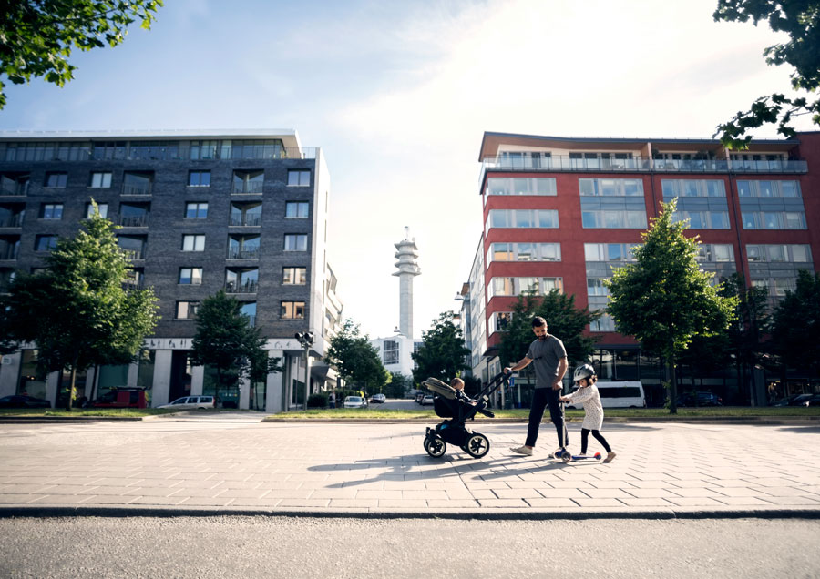 Pappa är ute och går med sina två barn framför lägenhetsområde